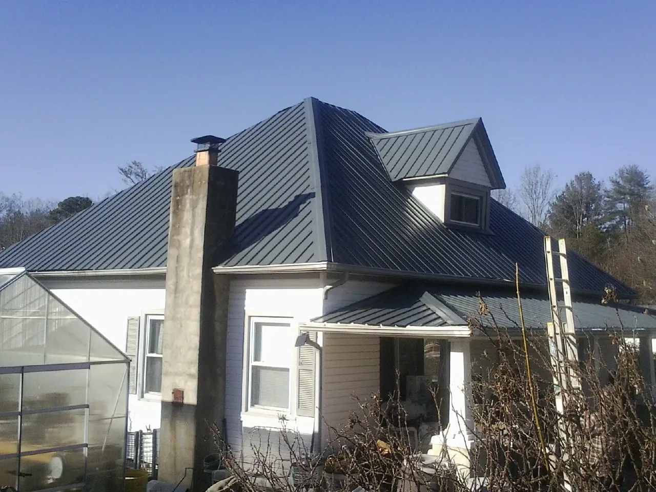 Dark blue standing seam metal roof on a white farmhouse with dormer — Slate & Tile Roof Repair by Roofing Brothers in Le Center