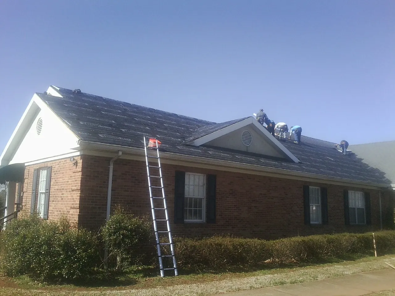 Crew tearing shingles off a brick ranch roof with a ladder set — Metal Roof Repair work by our crew in Le Center