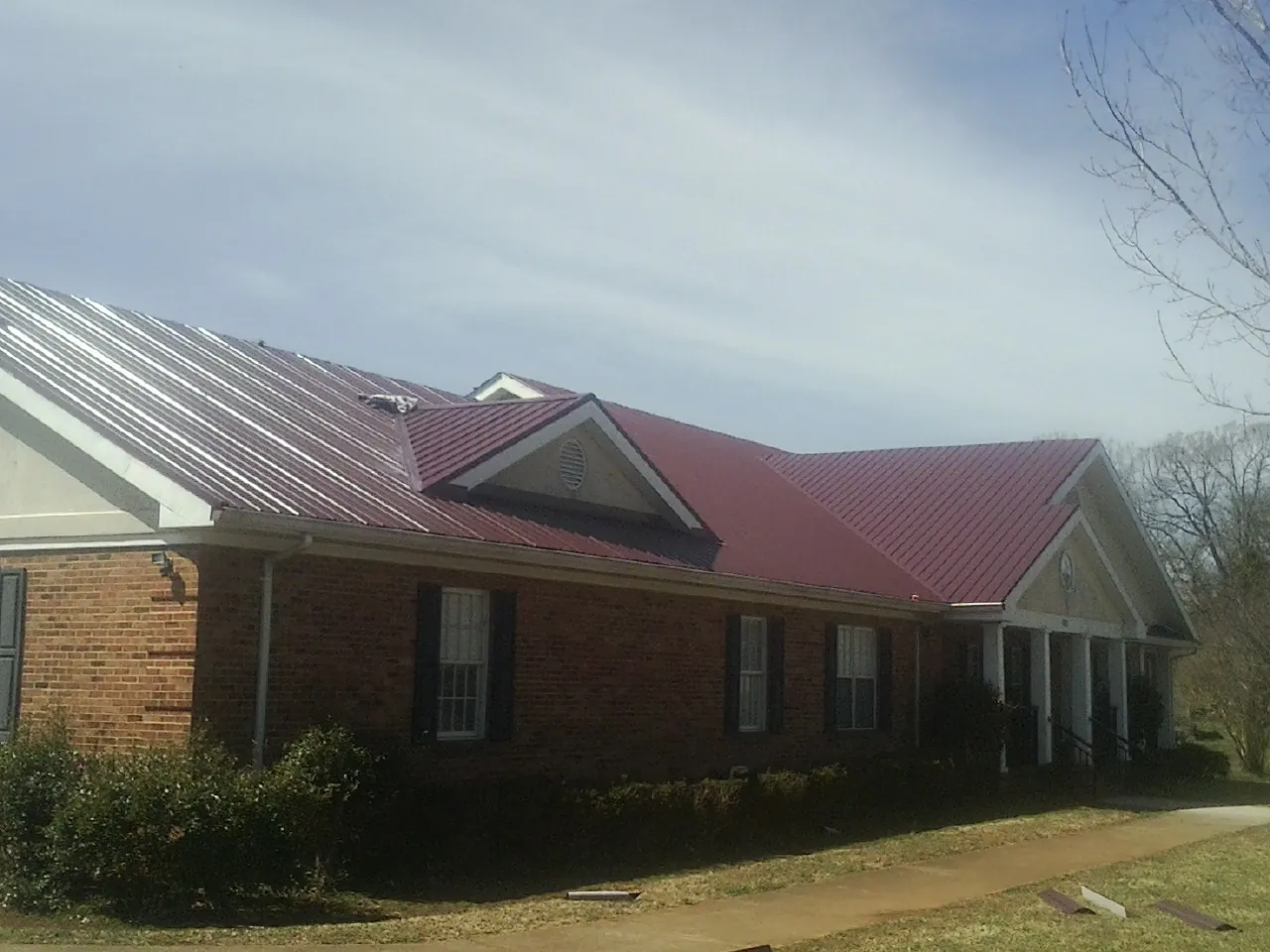 Red metal roof with gabled entries on a long brick building, from a Hail Damage Roof Repair job in Le Center