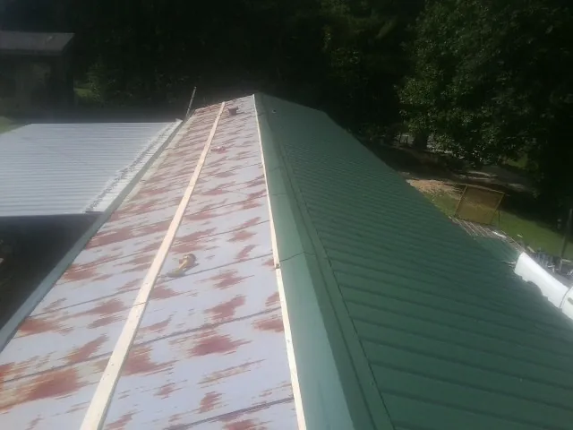 Old rusted panels beside newly installed green metal roofing — Wind Damage Roof Repair by Roofing Brothers in Le Center