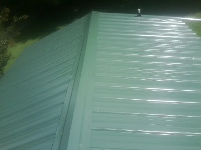 New green metal panels meeting at the ridge of a roof — Flat Roof Repair work by our crew in Le Center