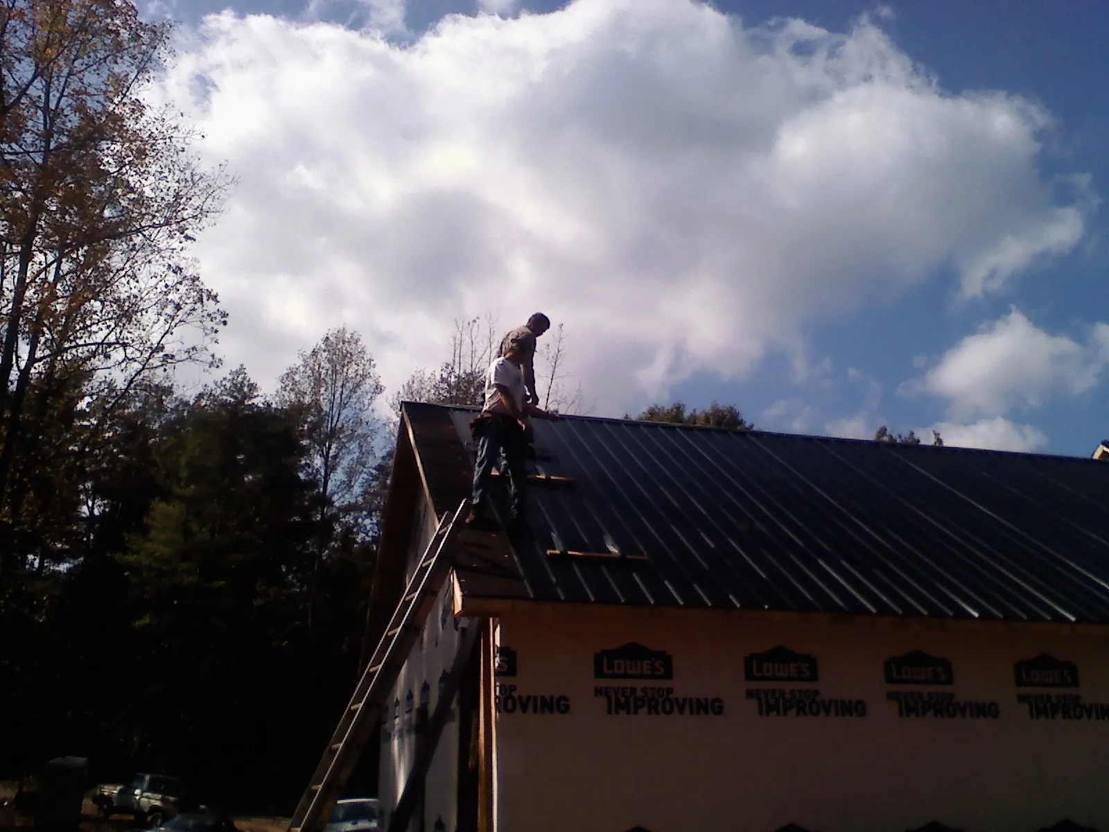 Roofer fastening dark metal panels high against a cloudy sky, from a Roof Inspection job in Le Center