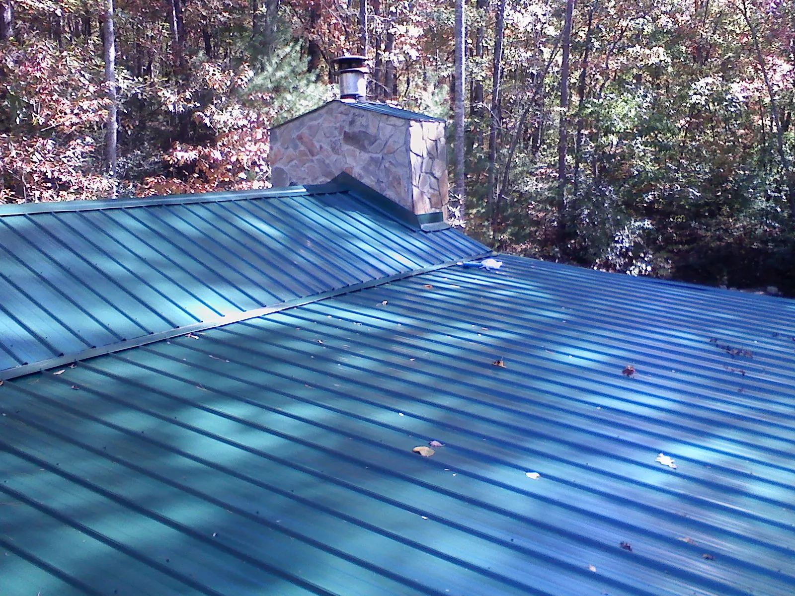 New green metal roof and stone chimney surrounded by autumn woods in Le Center