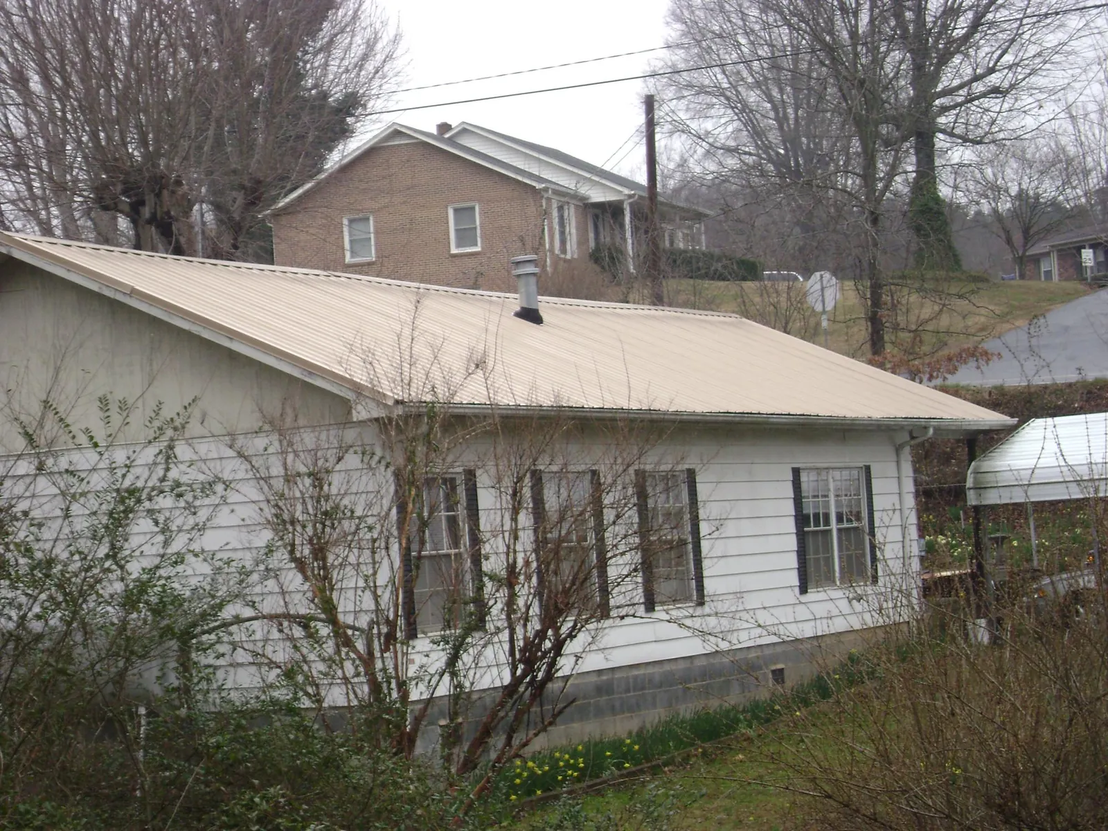 Tan metal roof on a white sided house set into a hillside — Commercial Roofing by Roofing Brothers in Le Center