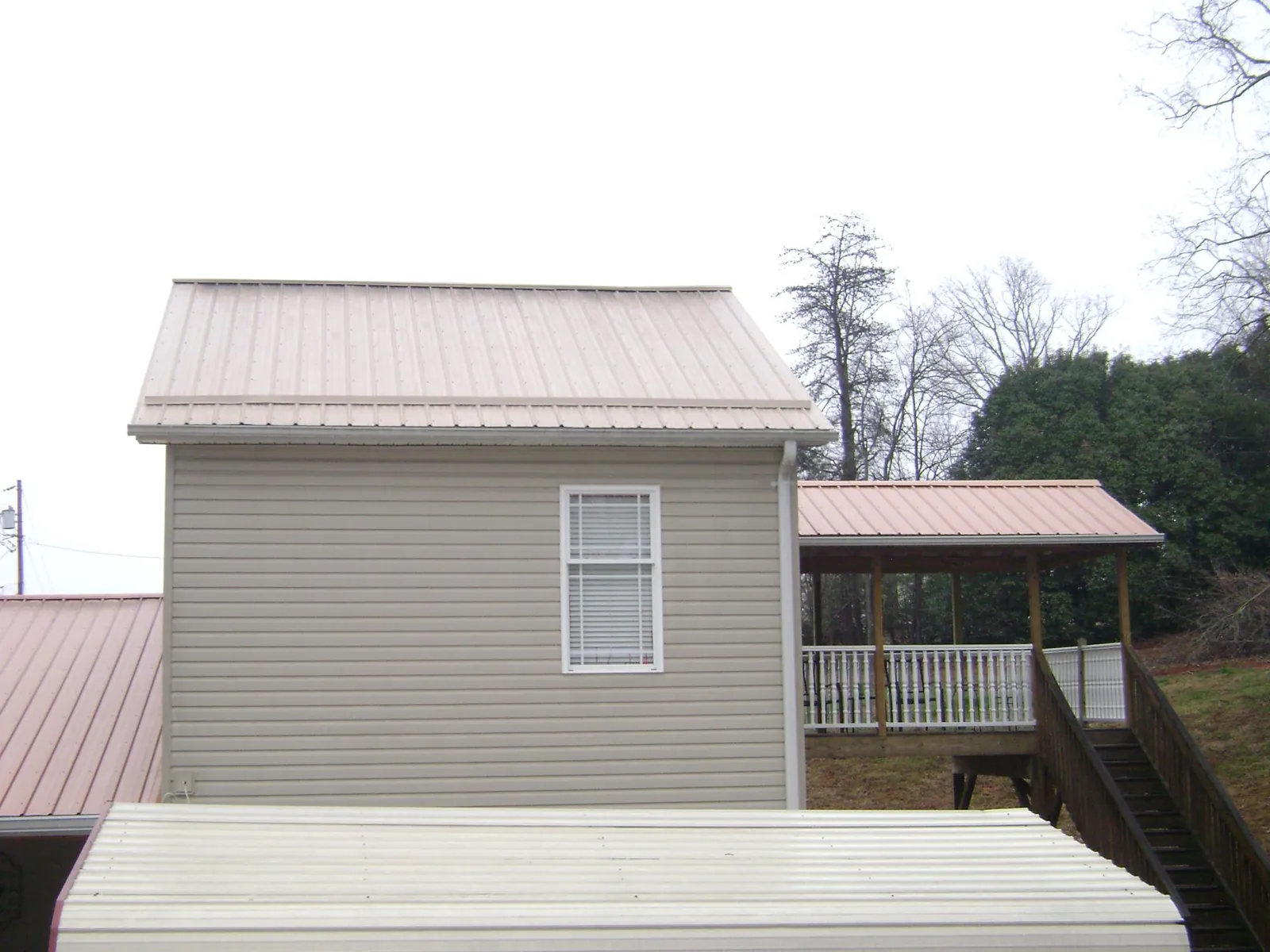 Tan metal roofs on a two story addition and attached porch, from a Roof Replacement job in Le Center